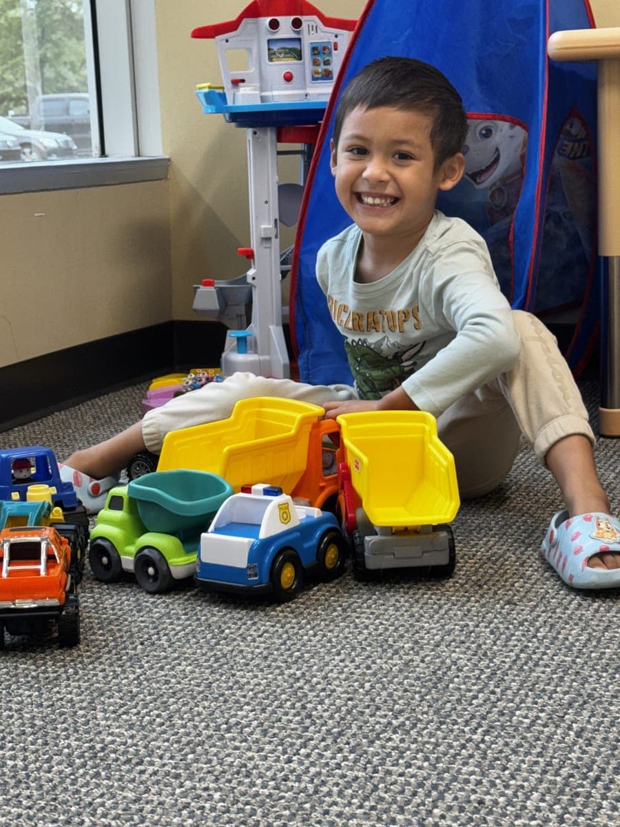 A smiling boy playing with toy trucks at a SEBS clinic